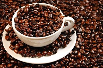 A white cup and saucer overflowing with roasted coffee beans