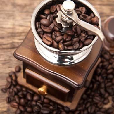 Roasted coffee beans piled in and around a wooden hand grinder