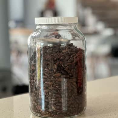 A glass jar of roasted cacao nibs standing on a counter